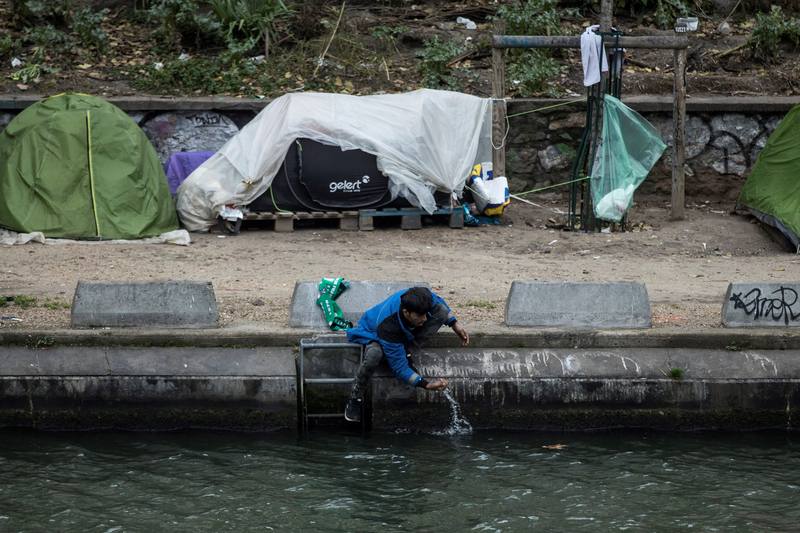 Un hombre se lava en un río frente a un campamento de inmigrantes en París