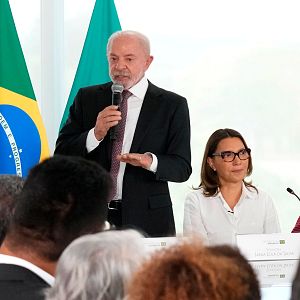 Hora América - Lula da Silva habla en un evento oficial, acompañado por Janja Lula da Silva y otra mujer. La bandera de Brasil ondea al fondo.