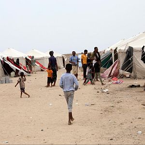 África hoy - Campamento de refugiados en terreno desértico con tiendas blancas y personas caminando por el pasillo central de tierra.