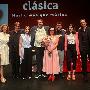 Sinfonía de la mañana - Nueve personas posan sonrientes sobre el escenario de un auditorio en Albacete, con el presentador Martín Llade en el centro y proyecciones de Radio Clásica al fondo.
