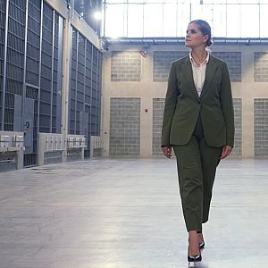 Hora América - Laura Fernández camina con traje verde oliva por un pasillo entre celdas en una moderna prisión.