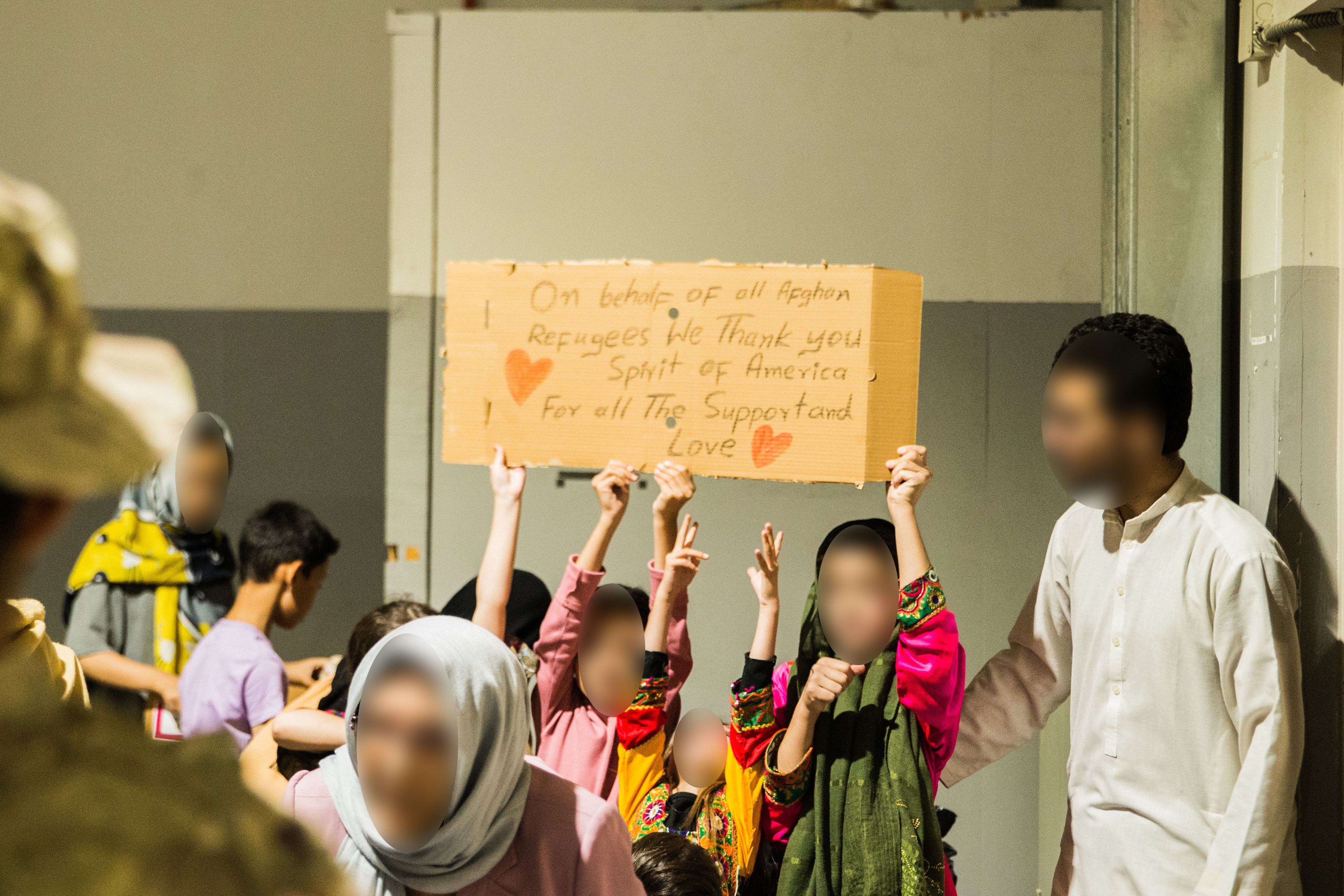 Un grupo de niños afganos levanta un cartel que dice “Gracias, América, por todo el apoyo y amor”. En el campamento reciben clases de inglés.