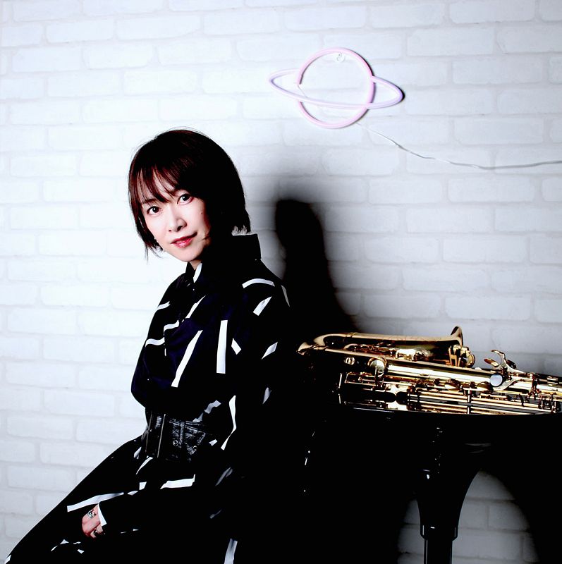 Saxofonista sentada junto a su instrumento dorado. Viste un vestido con rayas blancas y negras. Fondo con luz neón rosa.