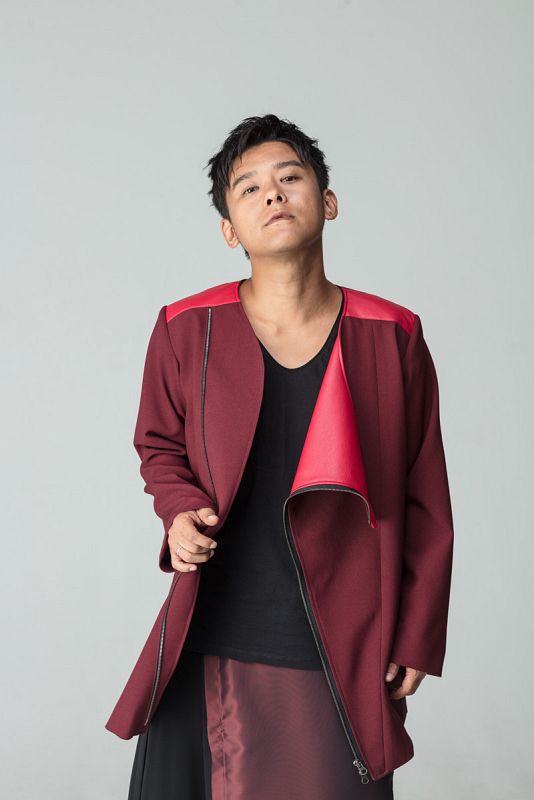 Hombre con chaqueta granate y detalles rojos, expresión seria, fondo gris claro.  Fotografía de moda con diseño vanguardista.