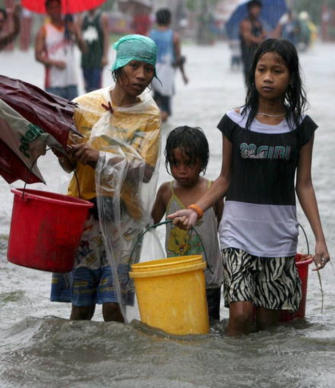 Una familia filipina cruzan una calle inundada por torrenciales lluvias en Las Pinas, sur de Manila