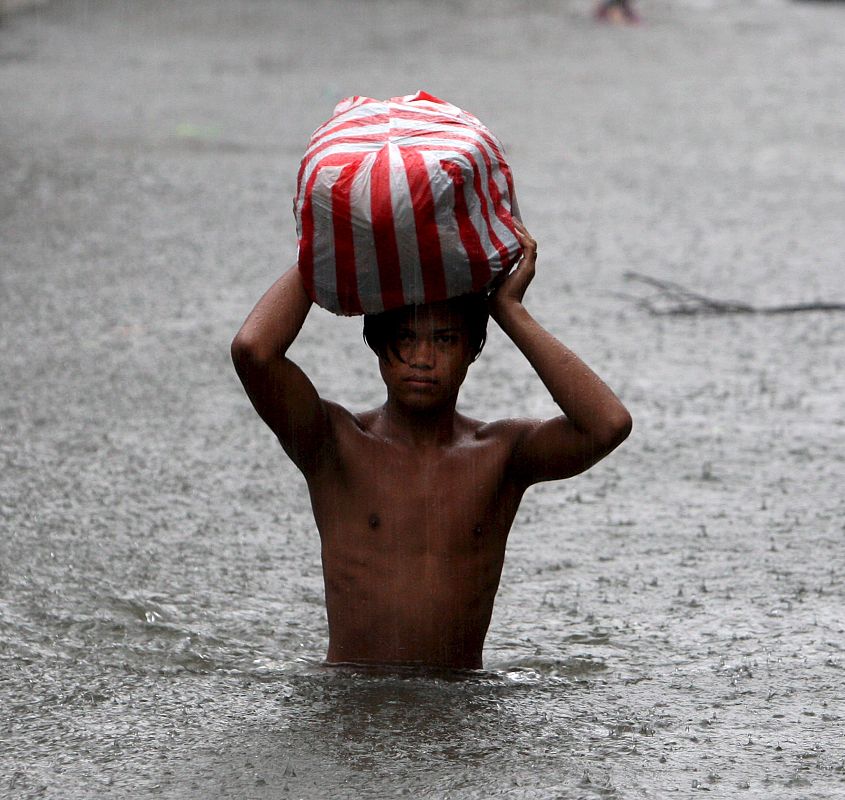 Un residente filipino cruza una calle inundada por torrenciales lluvias en San Juan, este de Manila, Filipinas