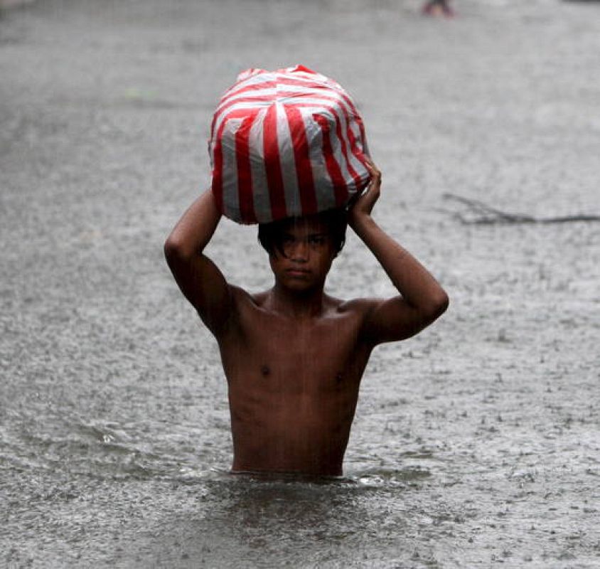 Un residente filipino cruza una calle inundada por torrenciales lluvias en San Juan, este de Manila, Filipinas  