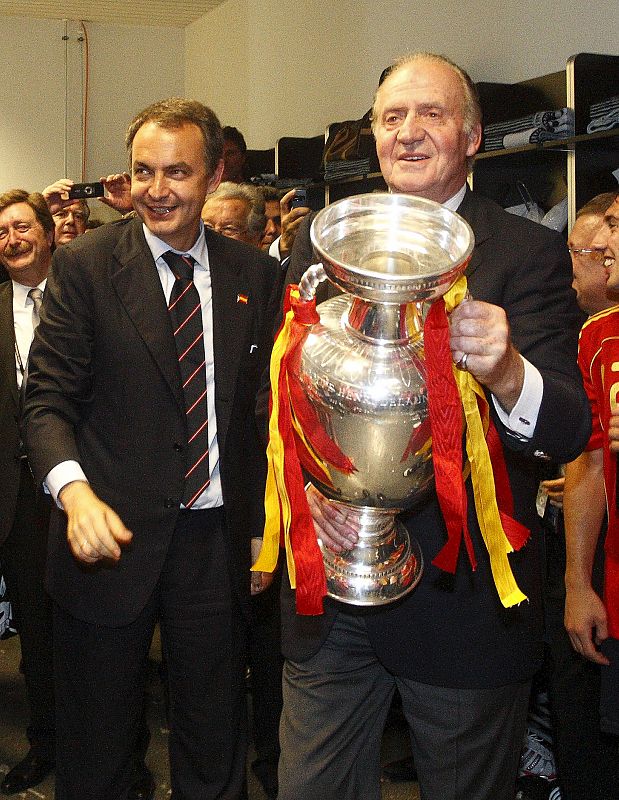 El rey Juan Carlos porta el trofeo de la Eurocopa '08 junto al presidente del Gobierno, José Luis Rodríguez Zapatero, en los vestuarios del equipo español tras la victoria en la final.