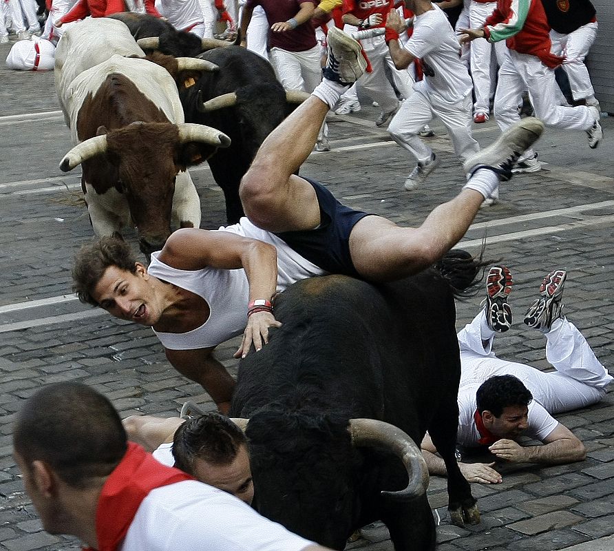 A runner falls on top of a fighting bull as they take the Estafeta curve during the third bull run of the San Fermin festival in Pamplona