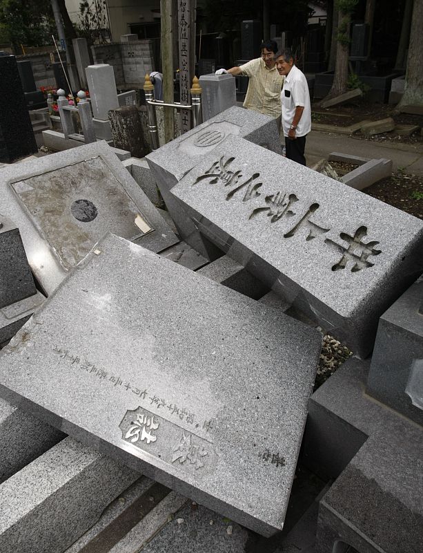 Varios japoneses miran los destrozos causados por un terremoto en un cementerio de Japón.