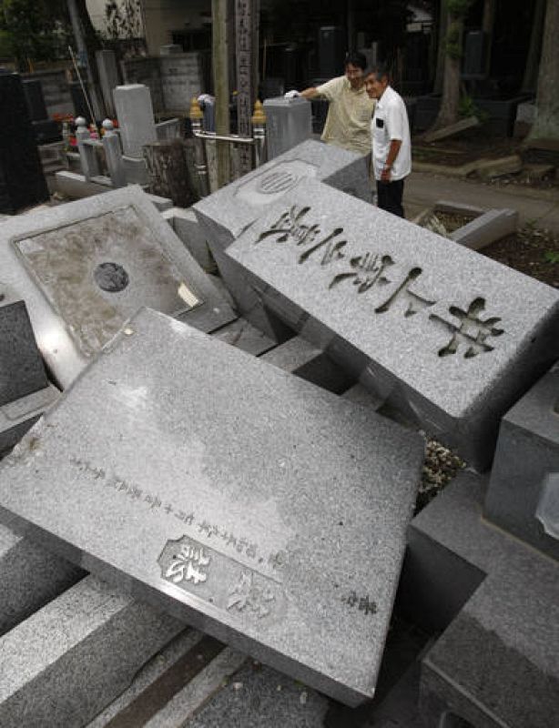 Varios japoneses miran los destrozos causados por un terremoto en un cementerio de Japón. 
