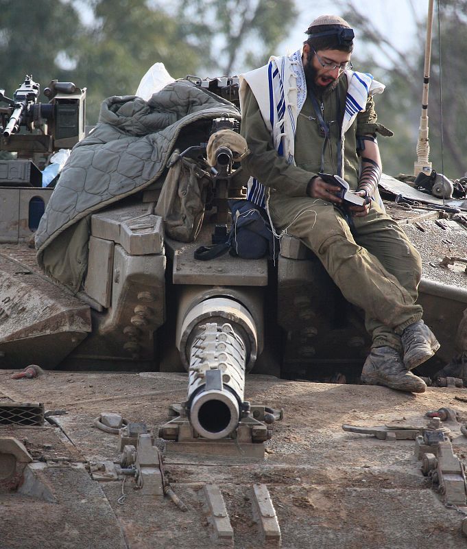 Soldados israelíes rezan en lo alto de un tanque mientras aguardan en la frontera para entrar en Gaza.