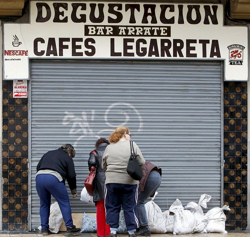 Varias mujeres ponen sacos en el exterior de un establecimiento, en Bilbao, para evitar la entrada de agua.