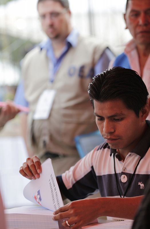 Un observador vigila la votación mientras un reponsable de mesa prepara las papeletas sin marcar en Panchimalco.