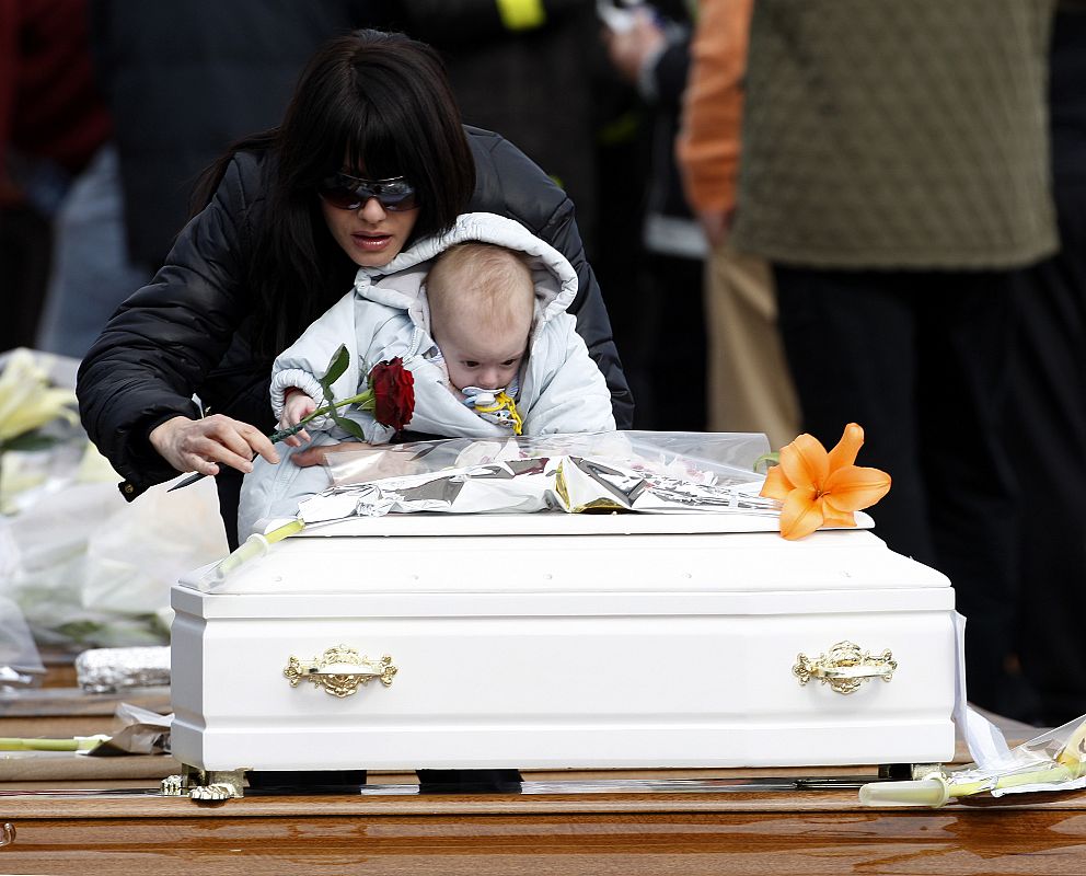 Una mujer y su hijo dejan una rosa sobre un pequeño féretro blanco en el funeral de Estado.