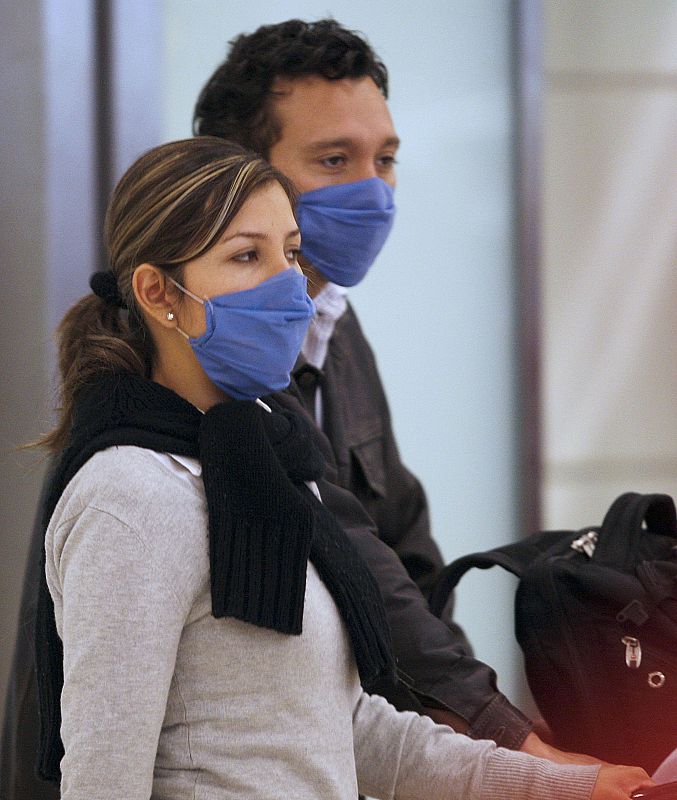 Una pareja transita por el aeropuerto de Madrid-Barajas con mascarillas ante el miedo a un posible contagio por gripe porcina.
