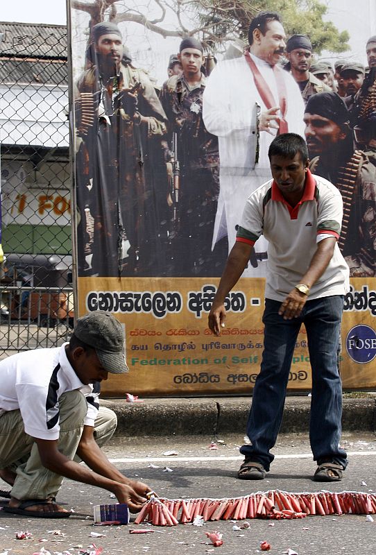 Dos hombres encienden fuegos artificiales frente a un cartel del presidente de Sri Lanka para celebrar la victoria.