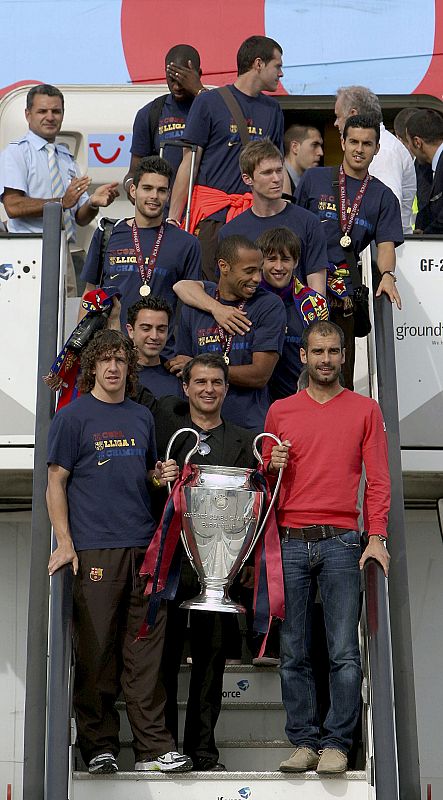 Guardiola, Puyol y el presidente Joan Laporta sostienen la copa junto al resto del equipo a su llegada al aeropuerto.