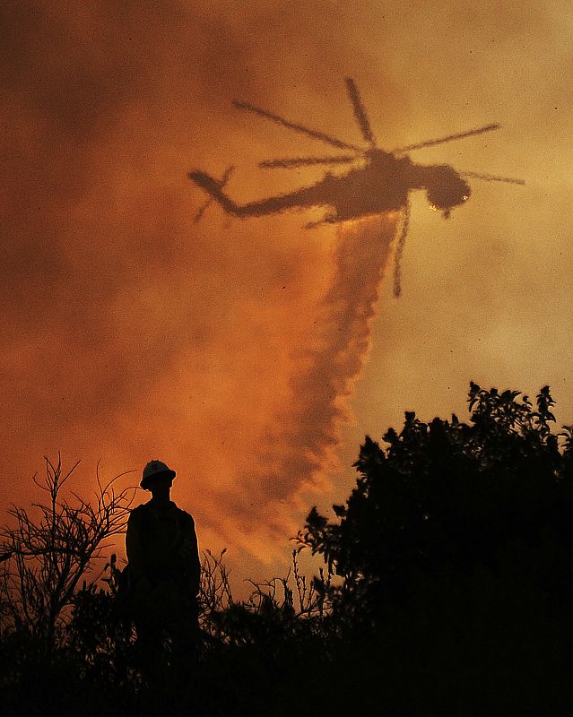 A firefighter watches a helicopter drop water on the Station Fire in Angeles National Forest above the La Canada Flintridge area of Los Angeles