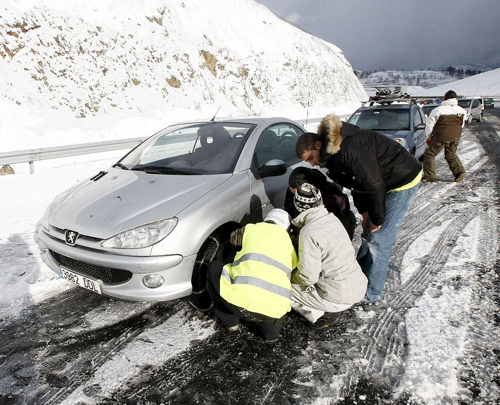 Varios conductores colocan las cadenas a uno de los vehiculos retenidos en la A-67 Autovia de La Meseta, que presenta graves problemas de circulación debido a las fuertes nevadas de las últimas horal producidas por una ola de frio polar.