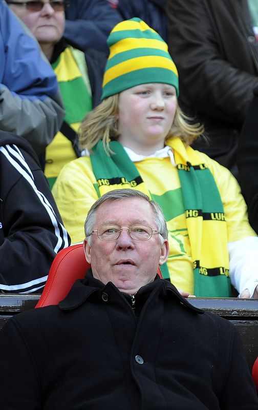 Alex Ferguson, técnico del Manchester, en su banquillo, observado por una aficionada 'anti-Glazer'.