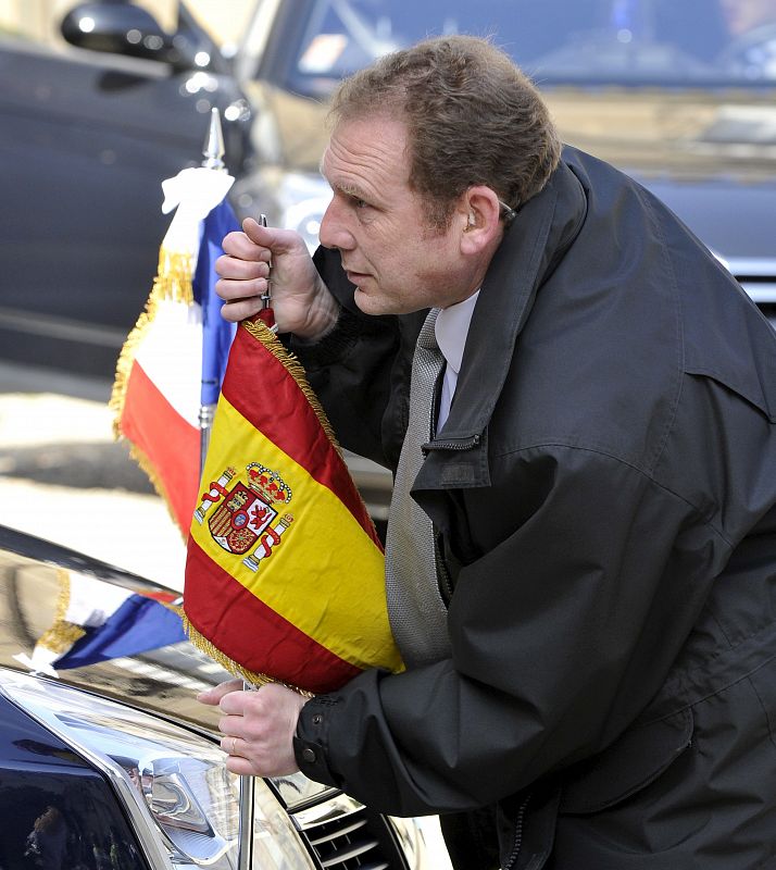 Un chófer coloca una bandera española junto a la francesa en el vehículo en el que Sarkozy y Zapatero para acudir a Melun al funeral.