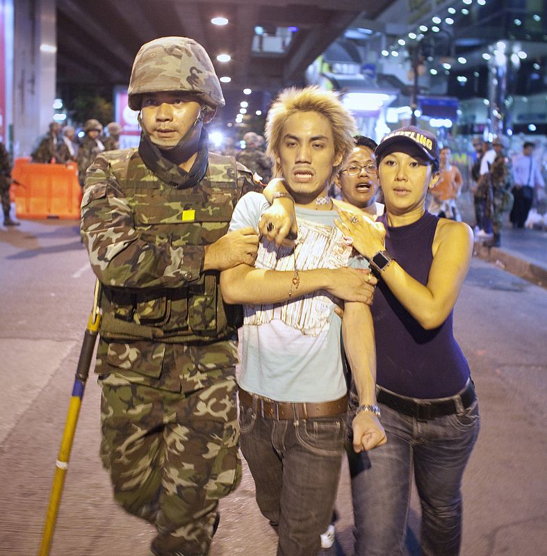 An army soldier and a woman assist an injured man to an ambulance after multiple explosions near pro-government supporters rallying in Bangkok's Silom business district
