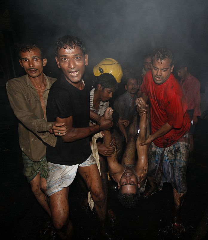 Locals and fire-fighters recover the body of a victim from the site of a fire in the old part of Dhaka