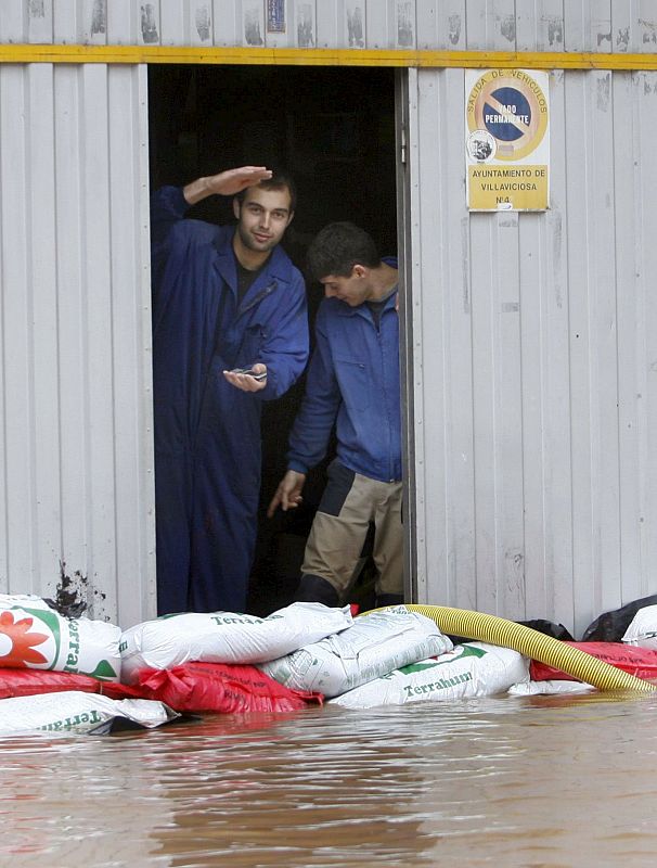 Un grupo de hombres protege con sacos de arena la entrada de un garaje, amenazada por una riada que ha inundado una de las calles de Villaviciosa, Asturias.