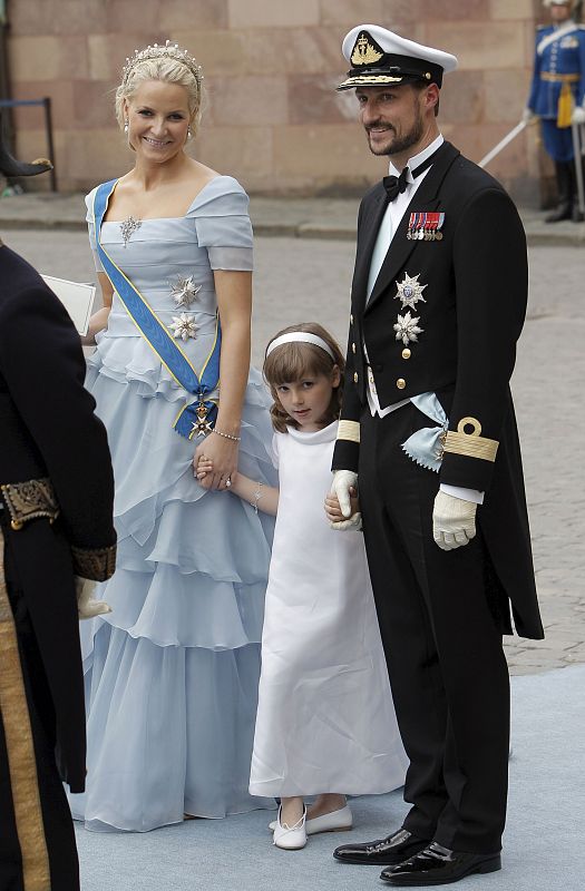 Los Príncipes Mette Marit y Haakon de Noruega y su hija Ingrid Alejandra. La Princesa luce un vestido en tono azul pastel, asimétrico y adornado con varios broches en el pecho y la cintura.