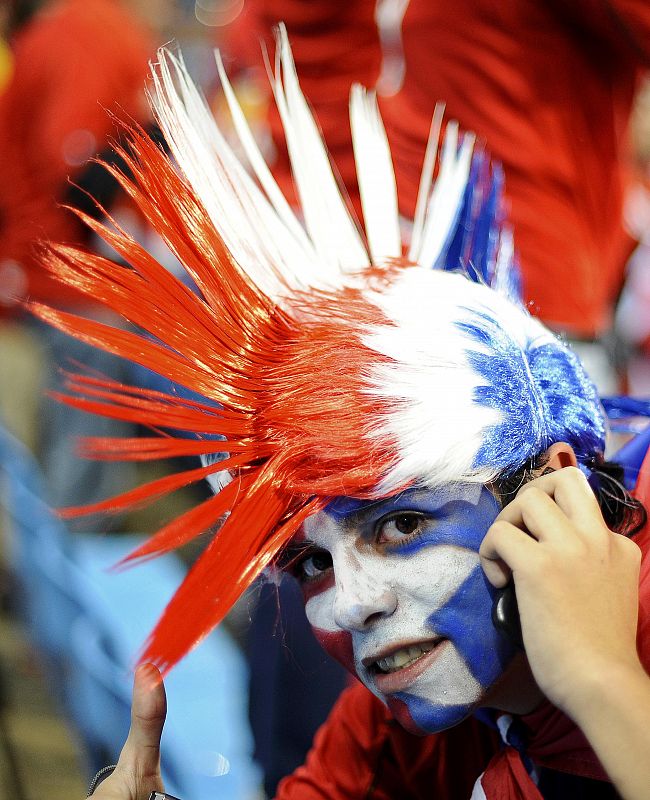 Un aficionado con una cresta con los colores de la bandera chilena mientras habla por télefono móvil.