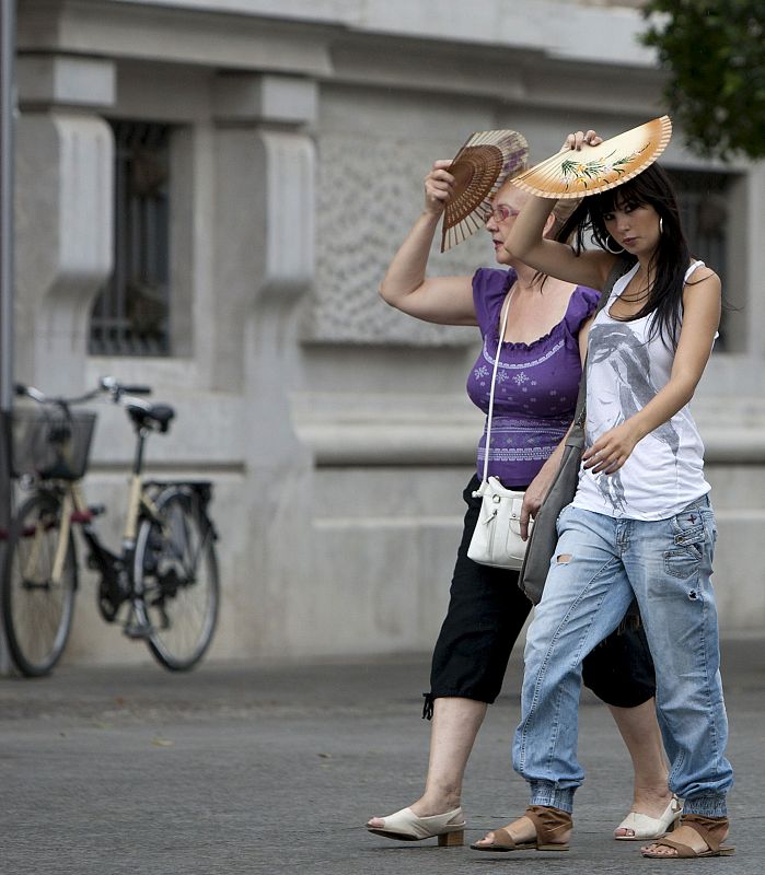 Dos mujeres se protegen con abanicos del chaparrón cayó ayer en Sevilla, a pesar de que la AEMET mantiene el nivel de alerta amarilla en la provincia.