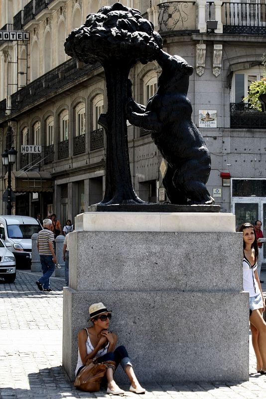 Una joven aprovecha la pequeña sombra sobre la base del monumento del "Oso y el Madroño", en la madrileña Puerta del Sol.