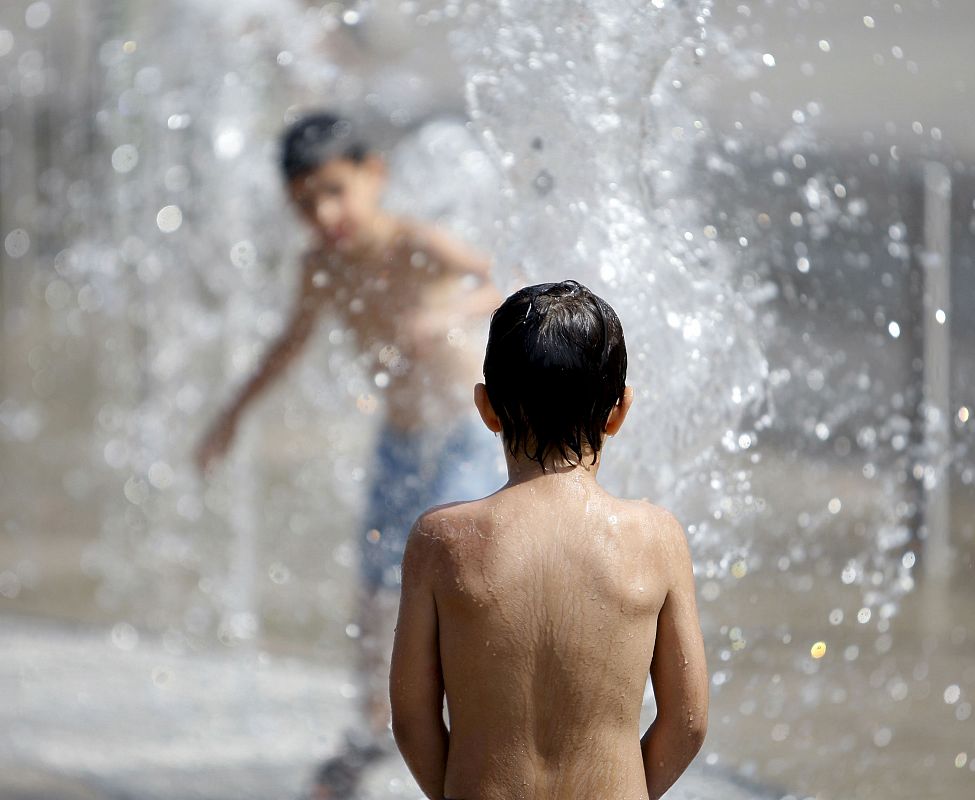 Unos niños se refrescan en una fuente en Bilbao, ya que la ola de calor no da tregua.