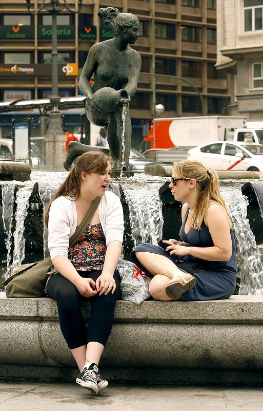 Estas dos madrileñas conversan sentadas en el borde de una fuente de la capital para combatir las altas temperaturas.