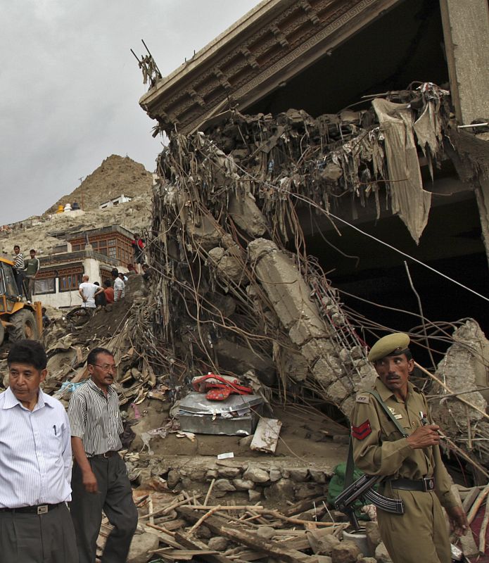 Soldados y civiles caminando al lado de una casa que se ha derrumbado tras las inundaciones en Leh