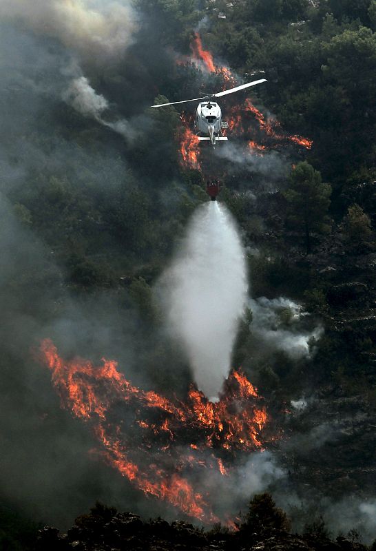 Un helicóptero descarga agua sobre el monte alrededor de Simat de Valldigna, donde están trabajando diversos medios aéreos y terrestres