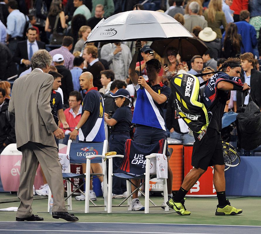 El tenista español Rafael Nadal (d) abandona el campo después de que el juez de la final del Abierto de Tenis de Estados Unidos, Brian Early (i), les solicitara a él y al serbio Novak Djokovic dejar la cancha debido al mal tiempo