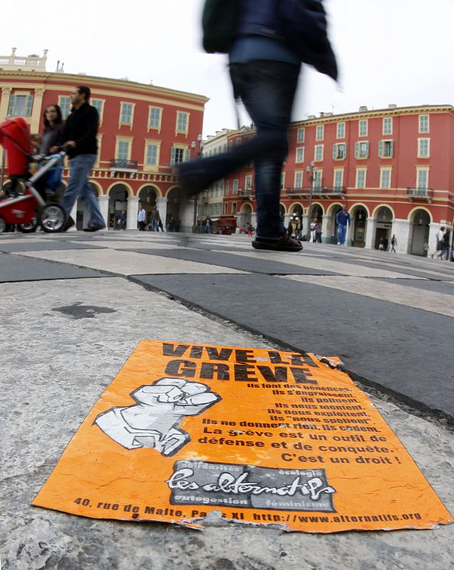 Passes-by walk past a sticker reading " Long live strike" in Nice