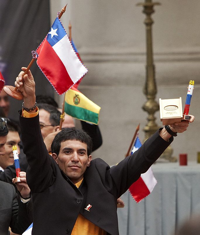 El minero Claudio Yáñez alza los brazos con la bandera chilena y una réplica de la cápsula de rescate que ha recibido en el homenaje ofrecido por el Gobierno en La Moneda.