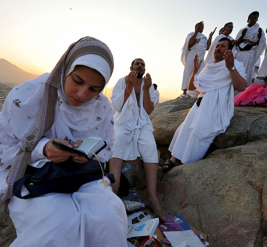 Una mujer lee el Corán mientras otros peregrinos musulmanes realizan el rezo de alba