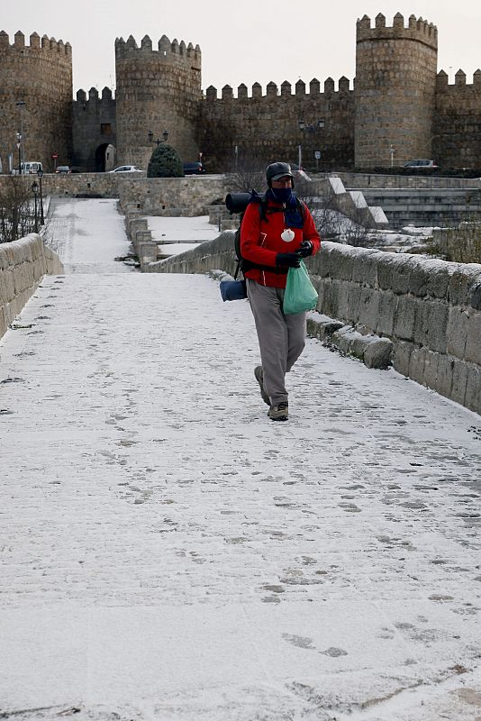 Un peregrino que recorre el camino de Santiago a su paso por Ávila, cubierta por la nieve. La nevada de las últimas horas en Castilla y León ha obligado a utilizar cadenas para transitar por seis puertos de Burgos, Salamanca y Palencia.