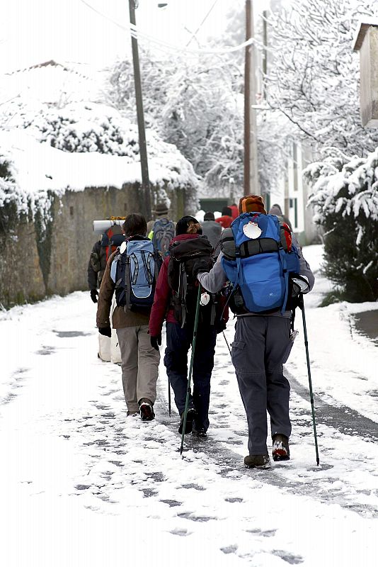 Varios peregrinos caminan con dificultad por un camino nevado, en la localidad de Palas de Rei. El temporal de frío y nieve permanecerá hasta el próximo miércoles, último día del puente de la Constitución.