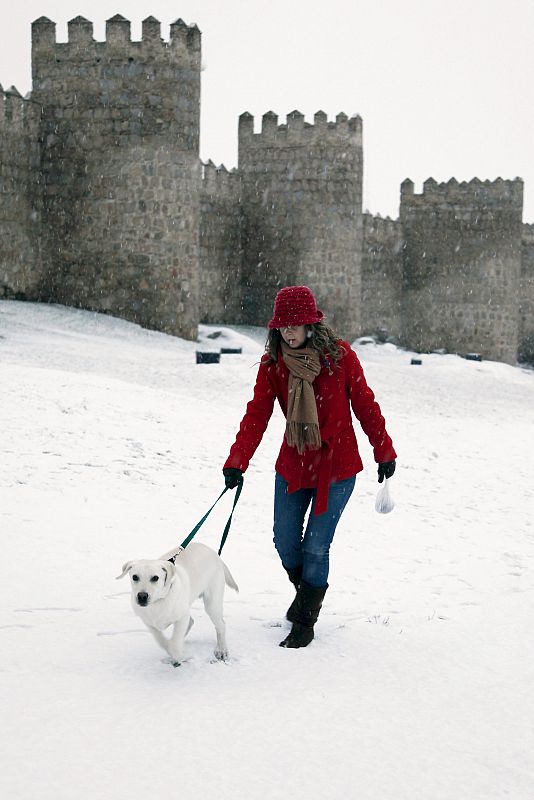 Una joven pasea con su perro sobre una densa capa de nieve, junto a la muralla de Ávila