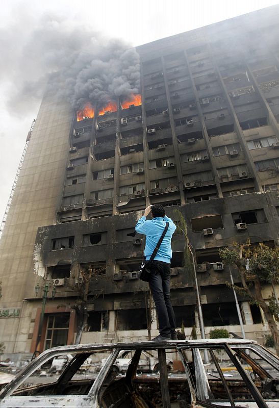 A youth takes photos of the burning building of the ruling National Democratic party in Cairo