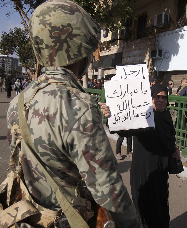 Una mujer se pasea delante de un soldado con un cartel en el que se puede leer "Mubarak, vete. Dios nos ayuda".