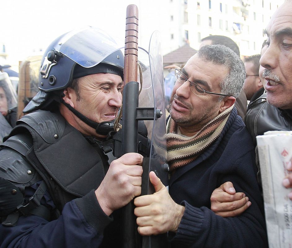 A riot policeman pushes against protesters as they chant slogans during a demonstration in Algiers