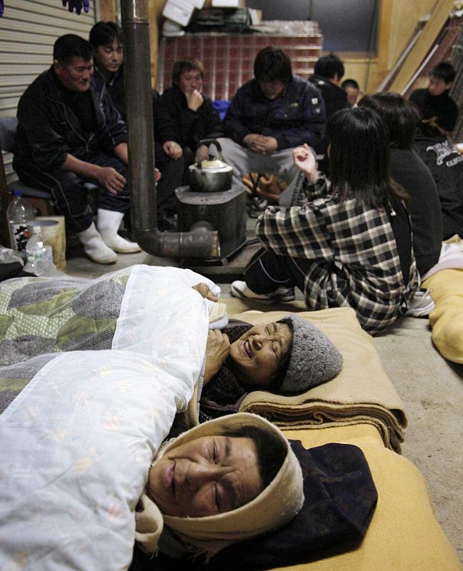 Women rest as other evacuees get warm around a wood-burning stove at an evacuation centre in Miyako