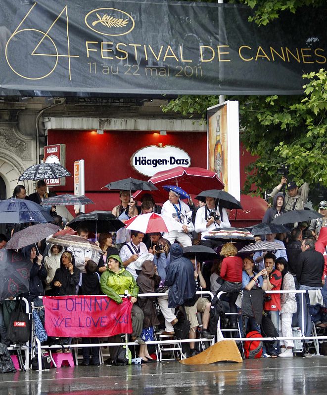 Fans protect themselves from the rain as they wait for the arrival of guests on the red carpet at the 64th Cannes Film Festival