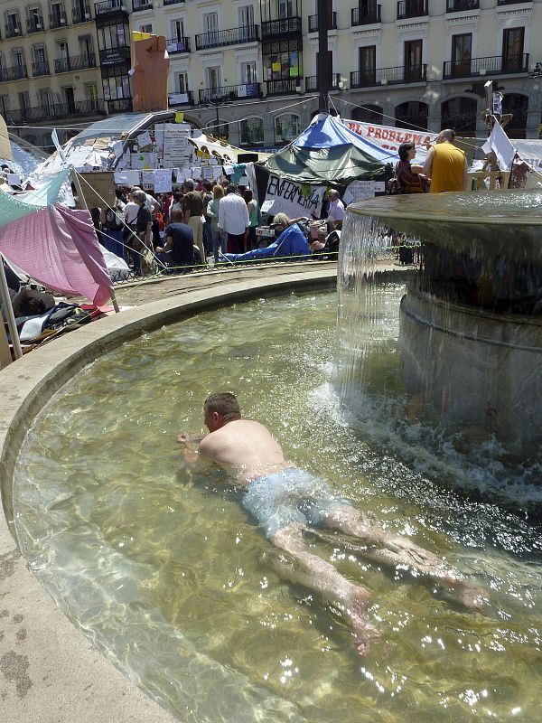 Los jóvenes que continúan acampados en la Puerta del Sol combaten el calor del mediodía en la fuente de la plaza.